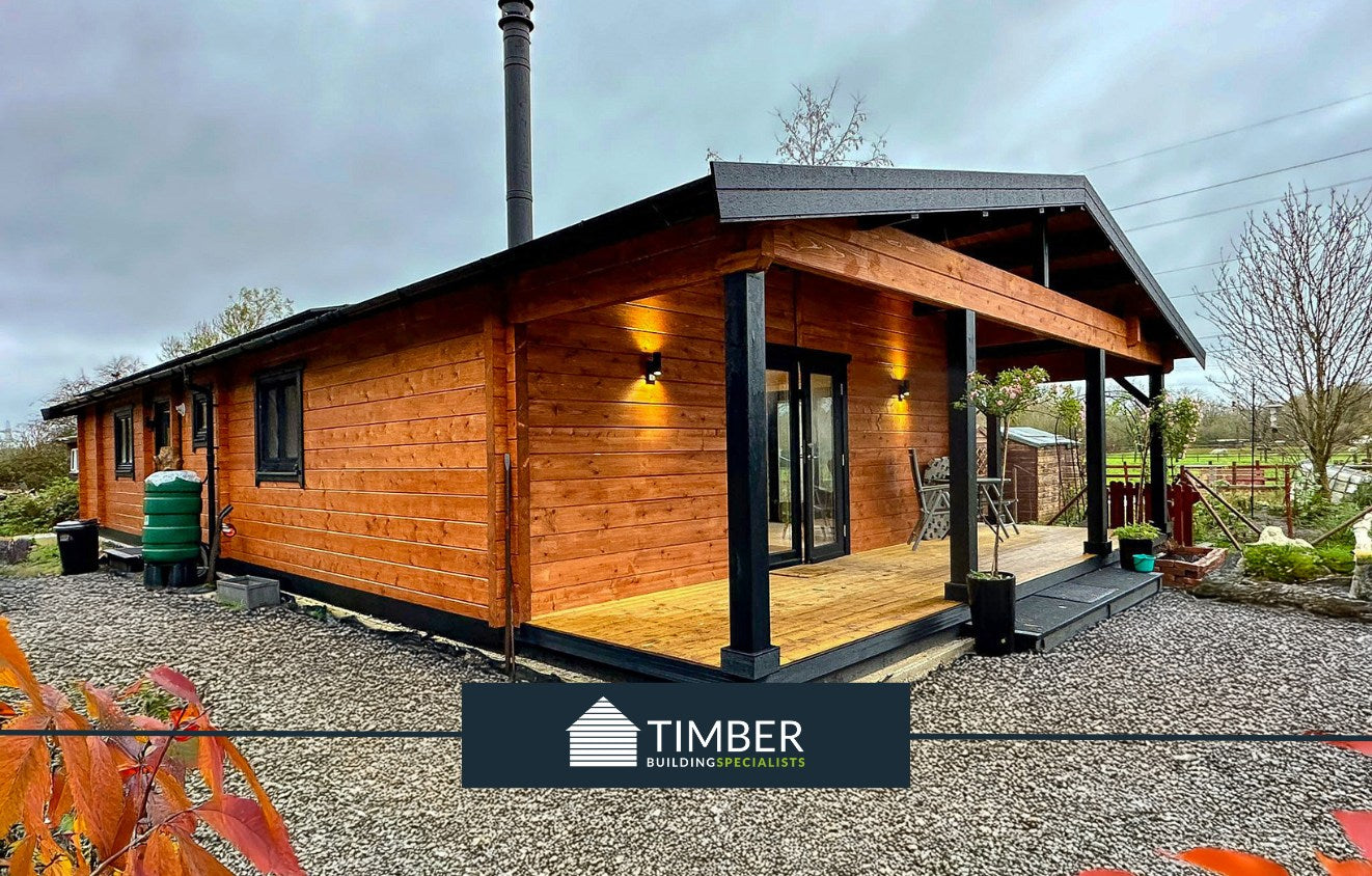 Modern timber log cabin with covered porch, exterior lights, and gravel pathway in garden setting