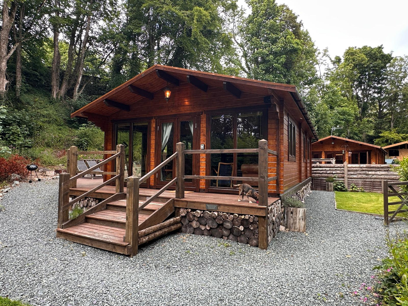 Wooden log cabin with front porch, gravel path, and surrounded by trees in a wooded setting