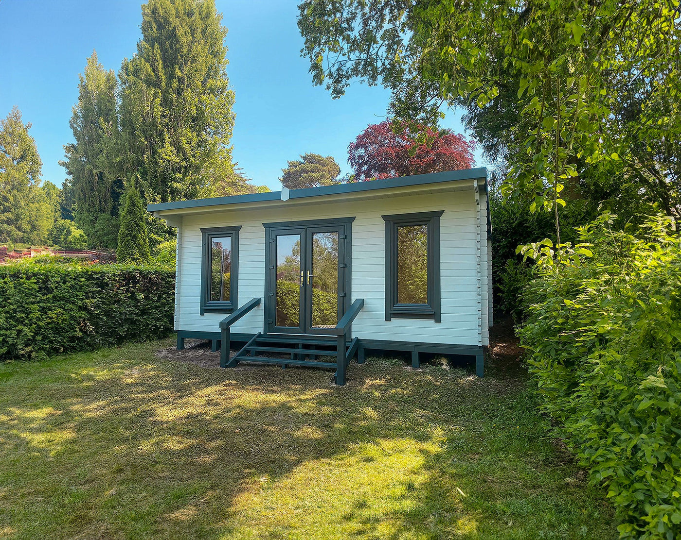 Modern timber log cabin home office with large windows in a lush garden setting