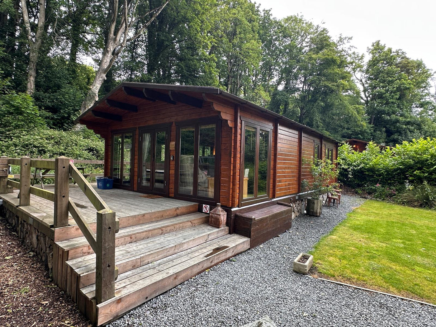 Modern timber log cabin with large windows and wooden deck in a lush forest garden