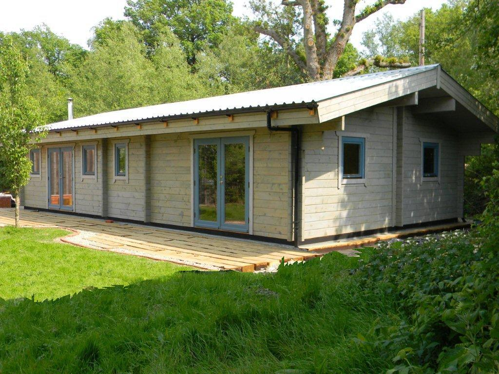 Modern timber log cabin with large windows and veranda in a green garden setting