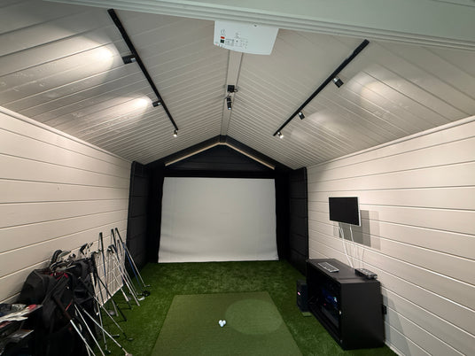 Indoor golf simulator setup with screen, projector, and golf equipment.