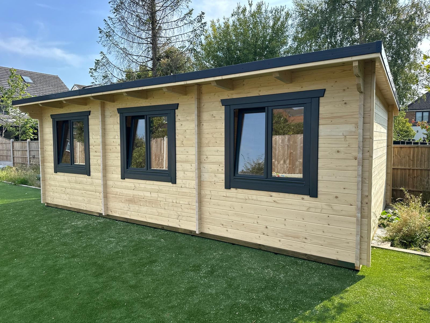 Large log cabin garden room with three windows and timber cladding on artificial lawn