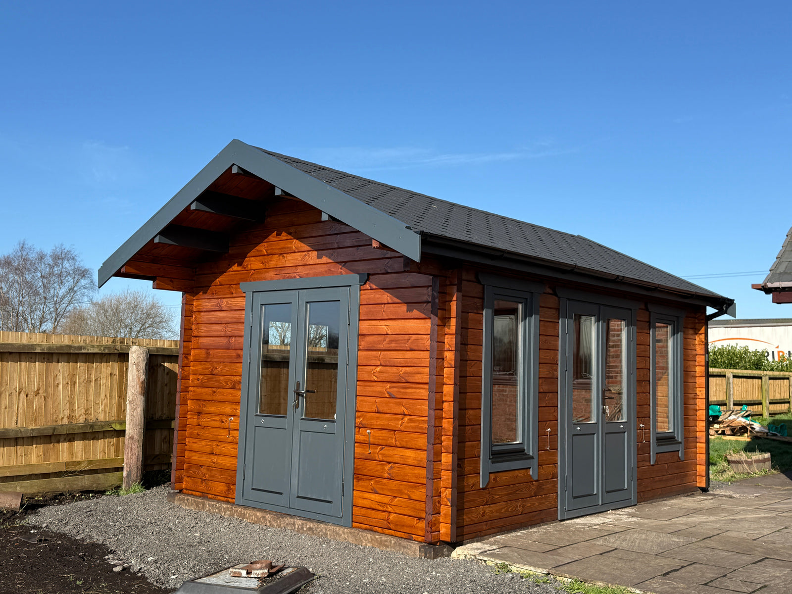 Modern timber log cabin with dark-framed windows and doors in a fenced garden