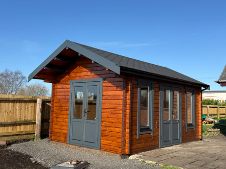Modern timber log cabin with dark-framed windows and doors in a fenced garden