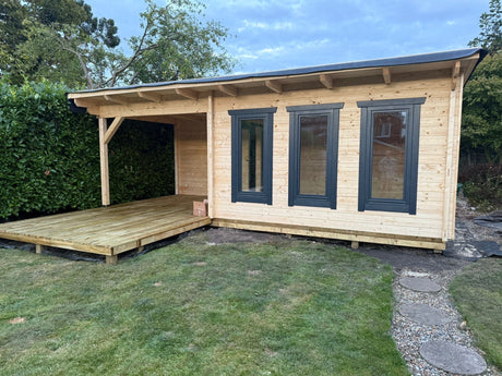 Modern timber log cabin with extended wooden deck set in a garden, featuring large windows.