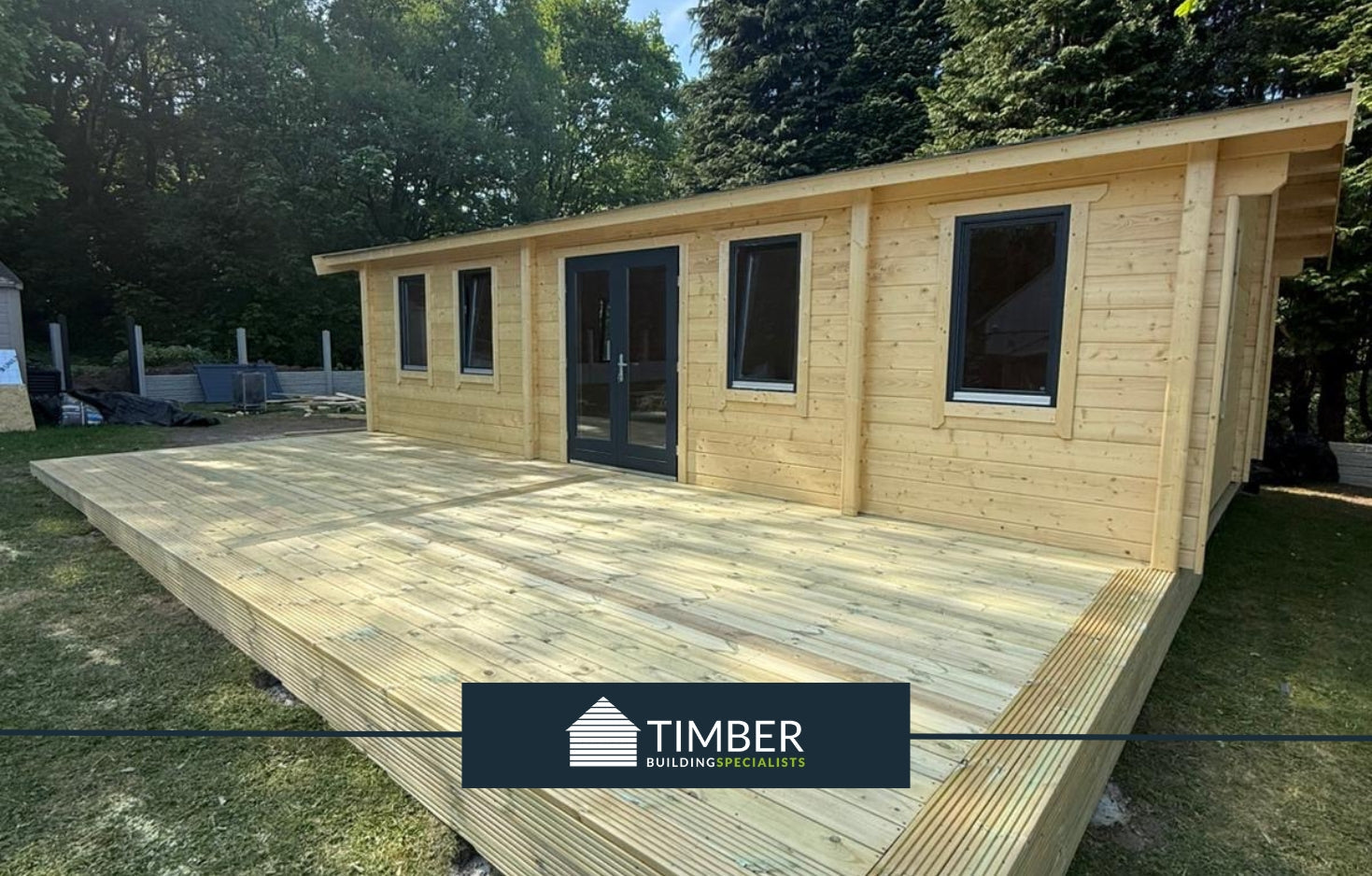 Modern timber log cabin with large windows and wooden deck in a forested garden.