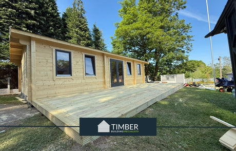Modern log cabin with large timber deck, set among trees in a garden setting