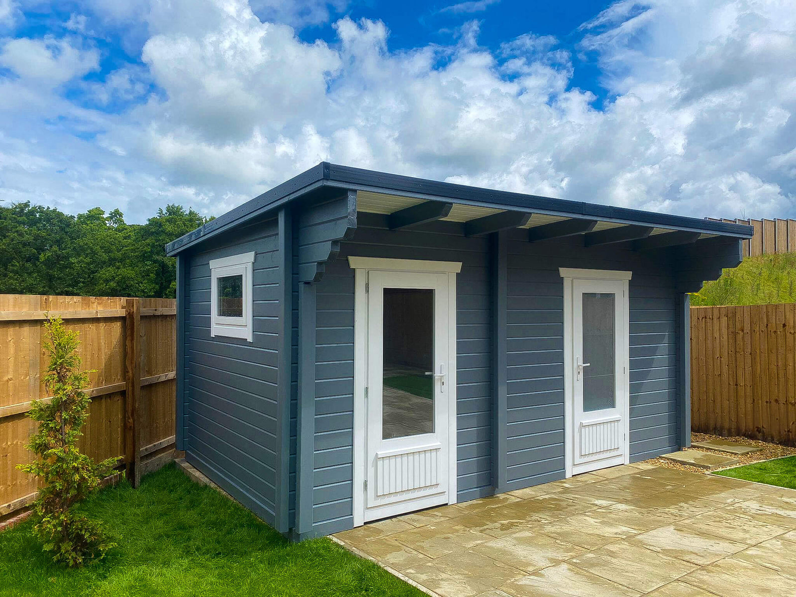 Modern blue timber garden office cabin with double doors, window, and flat roof in fenced yard