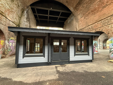 Modern log cabin with double doors and large windows under a brick archway with graffiti walls