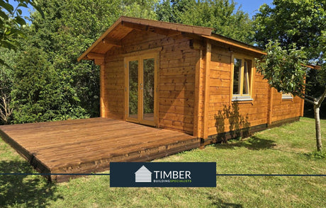 Timber log cabin with front deck in a green garden setting, large windows and double doors