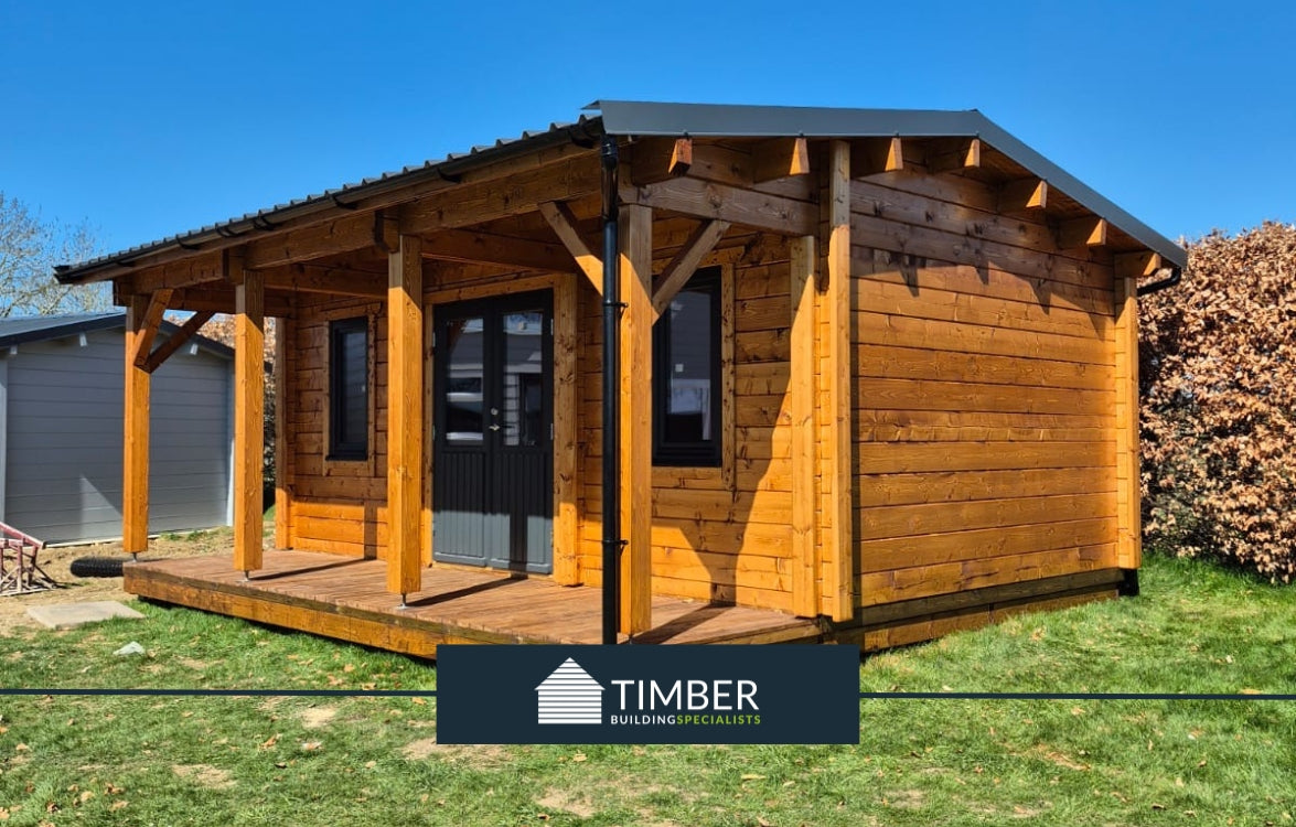 Wooden log cabin with porch, dark roof, and double doors in a grassy outdoor setting