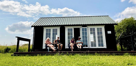 People relaxing outside a modern timber log cabin with double doors on a sunny day