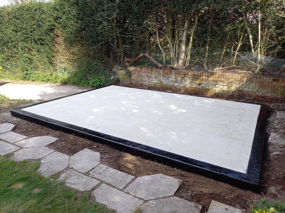 Concrete base with black rubber trim in garden, foundation for timber building or log cabin