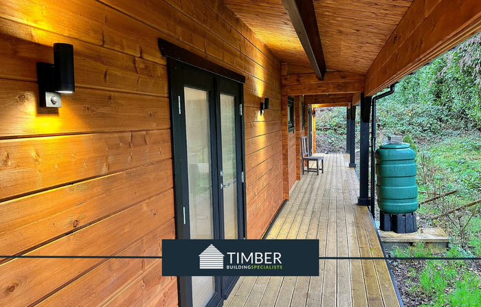 Modern log cabin exterior with covered timber veranda, outdoor lighting, and garden view